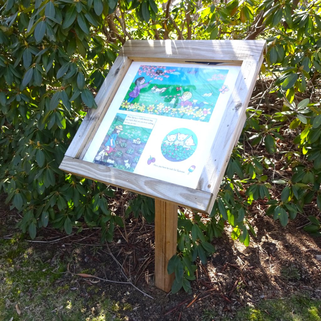 An image of one of the storywalk signs, backed by bushes.